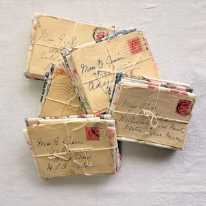 K&ouml;nnte beinhalten: Mehrere B&uuml;ndel antiker Briefe, mit Schnur zusammengebunden. Die Umschl&auml;ge weisen verblasste Handschrift, florale Muster und rote Briefmarken auf. Die Briefe sind auf einer wei&szlig;en Oberfl&auml;che angeordnet, was eine vergangene &Auml;ra andeutet.