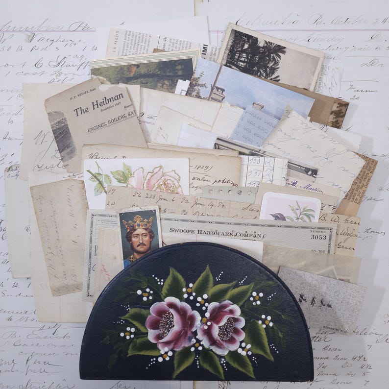 Pode incluir: Um recipiente preto, semicircular, com um desenho floral rosa e branco pintado &agrave; m&atilde;o, rodeado por pap&eacute;is antigos, postais e efem&eacute;rides. Os pap&eacute;is incluem notas manuscritas, documentos impressos e um retrato de um rei.