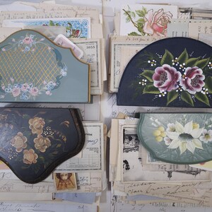 Pode incluir: Uma variedade de itens decorativos vintage pintados &agrave; m&atilde;o, incluindo um organizador de mesa, uma bandeja semicircular e duas outras bandejas. Os itens apresentam desenhos florais em tons de rosa, branco e dourado sobre um fundo azul e verde. Os itens est&atilde;o sobre pap&eacute;is antigos.