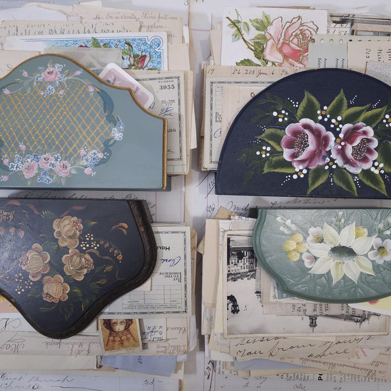 Pode incluir: Uma variedade de itens decorativos vintage pintados &agrave; m&atilde;o, incluindo um organizador de mesa, uma bandeja semicircular e duas outras bandejas. Os itens apresentam desenhos florais em tons de rosa, branco e dourado sobre um fundo azul e verde. Os itens est&atilde;o sobre pap&eacute;is antigos.