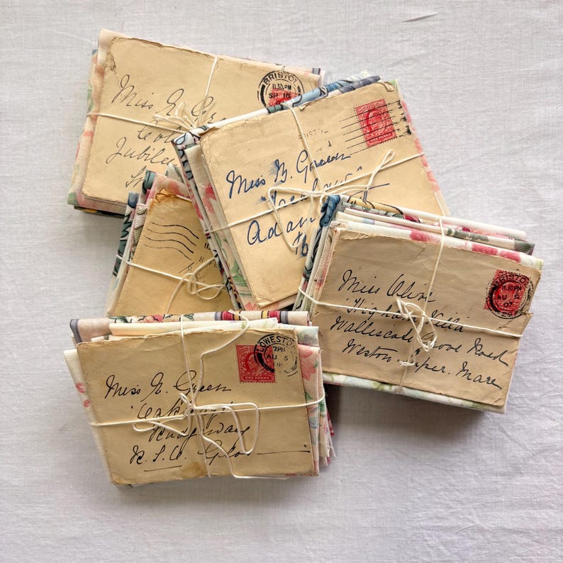 K&ouml;nnte beinhalten: Eine Sammlung von Vintage-Umschl&auml;gen, die mit Bindfaden zusammengebunden sind. Die Umschl&auml;ge sind in Kursivschrift beschriftet und weisen floral gemustertes Papier auf. Einige haben rote Briefmarken und Poststempel aus Bristol, England.