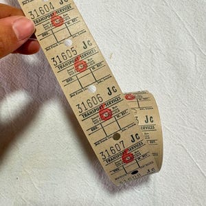 Könnte beinhalten: Eine fortlaufende Rolle aus beigefarbenen Transporttickets im Vintage-Stil mit schwarzem Aufdruck, darunter Transport Services, Bell Punch Co. Ltd, London, und fortlaufenden Nummern ab 31604, versehen mit kleinen runden Stanzlöchern und roten Stempeln.