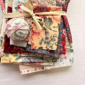 May include: A bundle of assorted floral fabric scraps tied with a cream-colored ribbon. The fabrics feature various floral patterns in red, yellow, blue, and white. A small fabric ball is also included in the bundle.