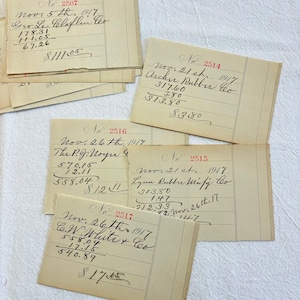 May include: A collection of five vintage off-white paper ledger slips from 1917, each featuring handwritten black ink entries, dates, company names like Geo. Le. Claflin Co., and numerical accounting calculations with specific invoice numbers in red ink.