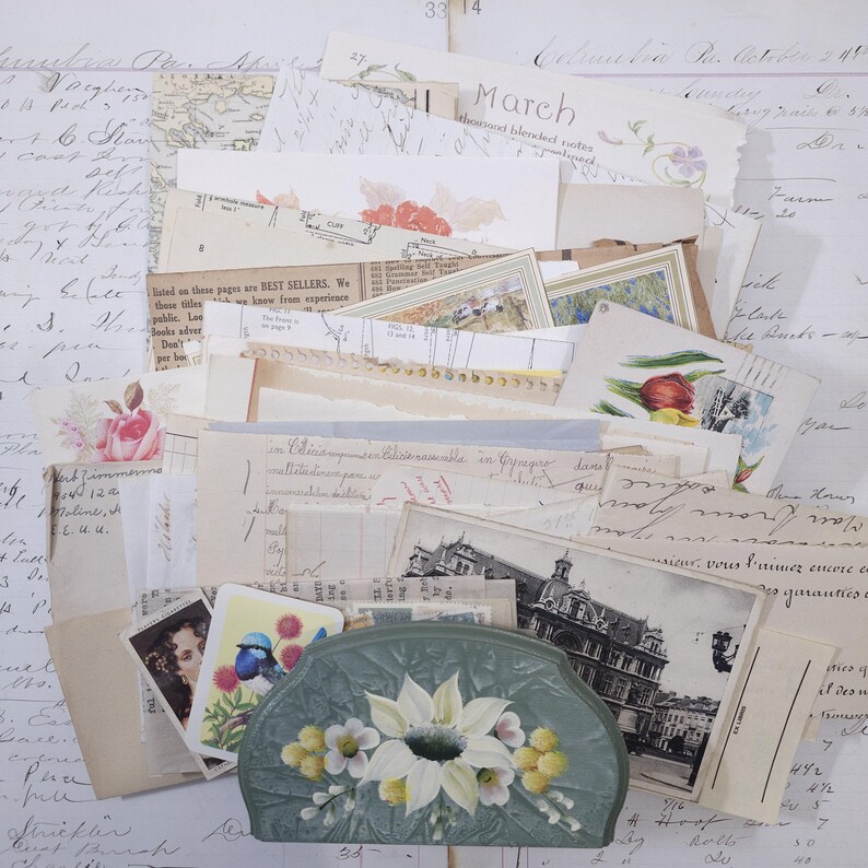 Pode incluir: Uma cole&ccedil;&atilde;o de ef&ecirc;meras vintage, incluindo postais, cartas manuscritas e ilustra&ccedil;&otilde;es florais. Uma clutch verde pintada &agrave; m&atilde;o com flores brancas e amarelas est&aacute; entre os pap&eacute;is. A palavra "March" &eacute; vis&iacute;vel.