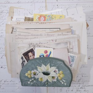 Pode incluir: Um organizador de secret&aacute;ria de estilo vintage em cor verde-azulado, adornado com um desenho de flor branca pintada &agrave; m&atilde;o. O organizador &eacute; preenchido com pap&eacute;is, cart&otilde;es e efem&eacute;rides envelhecidas, criando uma est&eacute;tica nost&aacute;lgica.