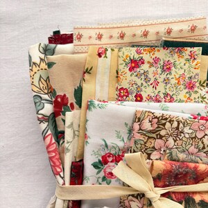 May include: A bundle of assorted fabric swatches in various floral patterns and colors, including red, pink, yellow, and green. The fabrics are tied together with a beige ribbon. The bundle includes a variety of textures and designs, perfect for crafting or sewing projects.