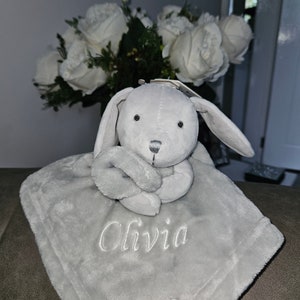 May include: A gray plush bunny with a gray blanket. The blanket has the name "Olivia" embroidered on it.