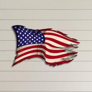 May include: A distressed American flag wall decor in red, white and blue. The flag is tattered and torn, giving it a rustic and vintage look.