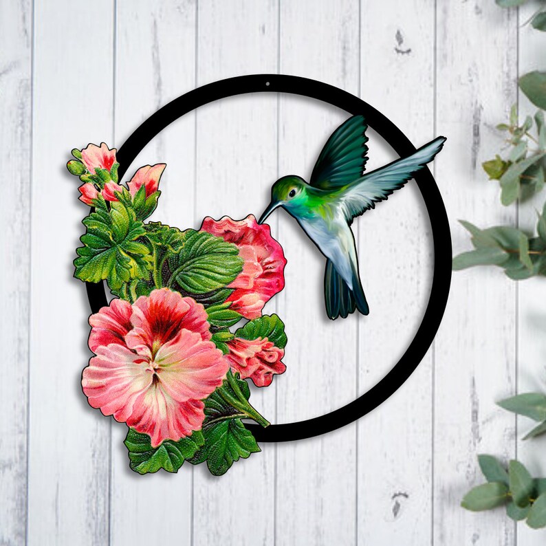 May include: A black metal circle with a hummingbird in flight, drinking nectar from pink flowers. The hummingbird is green, blue, and white. The flowers are pink and white with green leaves.