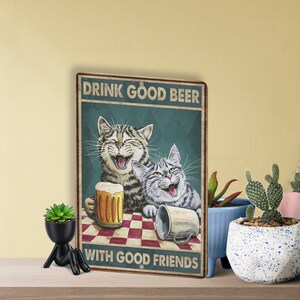 May include: A vintage-style poster with two cats laughing and holding drinks. The text reads "Drink good beer with good friends".