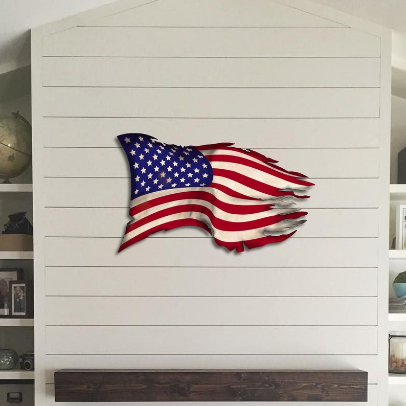 May include: A distressed American flag wall decor in red, white and blue. The flag is tattered and torn, giving it a rustic and vintage look.