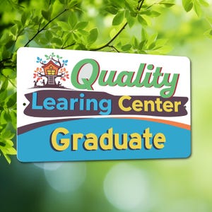 May include: A rectangular sign with the words "Quality Learning Center Graduate" in green, yellow, and blue. The sign has a treehouse graphic and is set against a blurred green background.