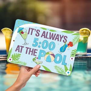 May include: A blue and green metal sign with the text "It's Always 5:00 At The Pool" in white. The sign features a beach ball, a cocktail glass, and tropical leaves.
