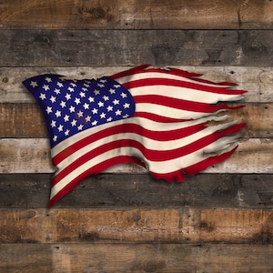 May include: A tattered American flag with red, white and blue stripes and stars, hanging against a weathered wooden background.