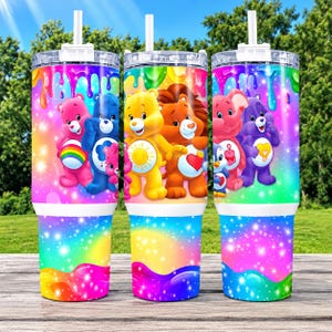 May include: Three stainless steel tumblers with clear lids and straws, featuring a vibrant rainbow gradient background with dripping paint effects and sparkling star patterns. The tumblers display colorful cartoon bears and animals.