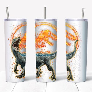 May include: A white stainless steel tumbler with a blue and orange dinosaur graphic. The dinosaur is roaring with its mouth open. The graphic also includes a circle with a dinosaur skeleton inside. The tumbler has a straw.