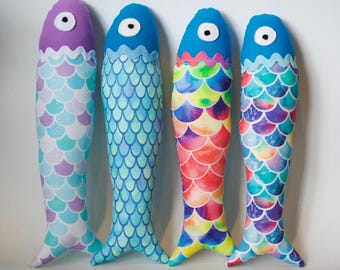 May include: Four fish-shaped plush toys in various colours. Each has a different scale pattern in shades of blue, purple, and rainbow. The fish have a blue or purple head with a white eye and a small tail fin.