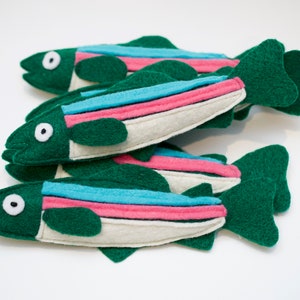 May include: A set of four felt fish toys in green, white, pink, and blue. The fish have a simple design with a single eye and a fin on each side.