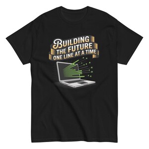 以下が含まれることがあります： 黒いTシャツ。ノートパソコンと緑色の線が描かれています。ノートパソコンの上には、スタイリッシュなフォントで「Building the Future One Line at a Time」というテキストがあります。