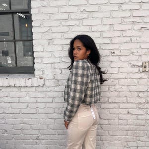 May include: A woman wearing a cropped plaid jacket against a white background. The jacket has a black and white check pattern. The woman is wearing beige trousers.