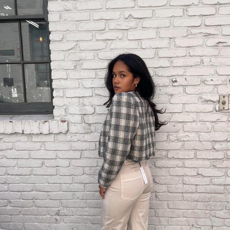 May include: A woman wearing a cropped plaid jacket against a white background. The jacket has a black and white check pattern. The woman is wearing beige trousers.