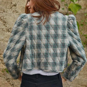 May include: A cropped quilted jacket with a plaid pattern in shades of green and beige. The jacket has puffed sleeves and a relaxed fit.