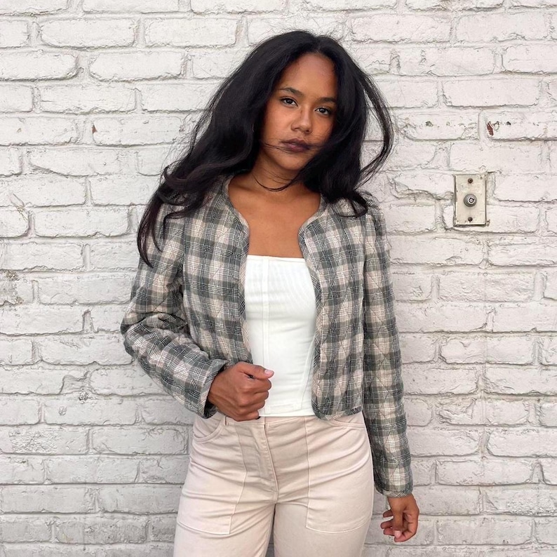 May include: A woman wearing a cropped plaid jacket with a white vest top and beige trousers. The jacket has a slightly oversized fit and a relaxed silhouette.