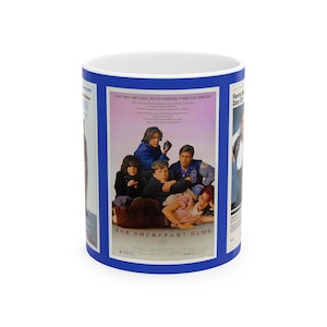 May include: A white ceramic mug with a blue rim and handle. The mug features a movie poster design for "The Breakfast Club." The poster shows a group of teenagers and the text "THE BREAKFAST CLUB."