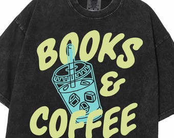 May include: A black acid-wash t-shirt featuring the text BOOKS & COFFEE in a light yellow font. Centered between the words is a graphic of a light blue iced beverage in a clear cup with a straw and ice cubes, outlined in a darker blue color.
