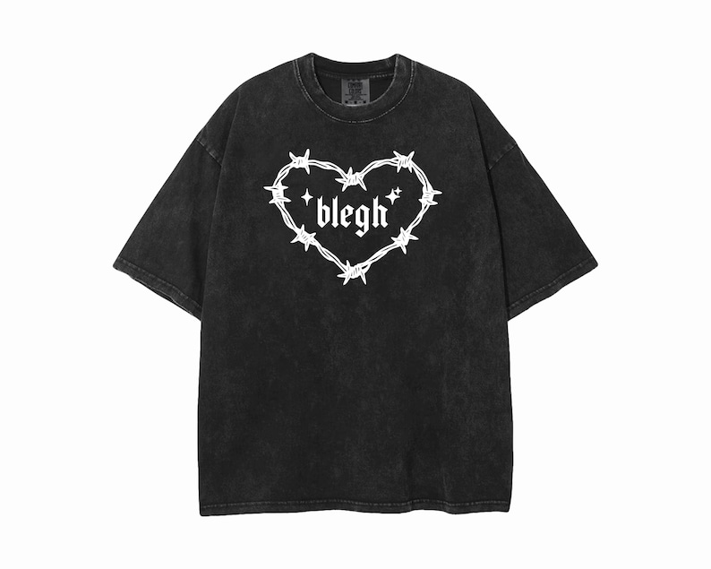May include: A black acid-wash t-shirt featuring a white graphic print on the chest. The design consists of a heart shape formed by barbed wire with the word blegh written in a gothic font inside, accompanied by two small four-pointed star icons.