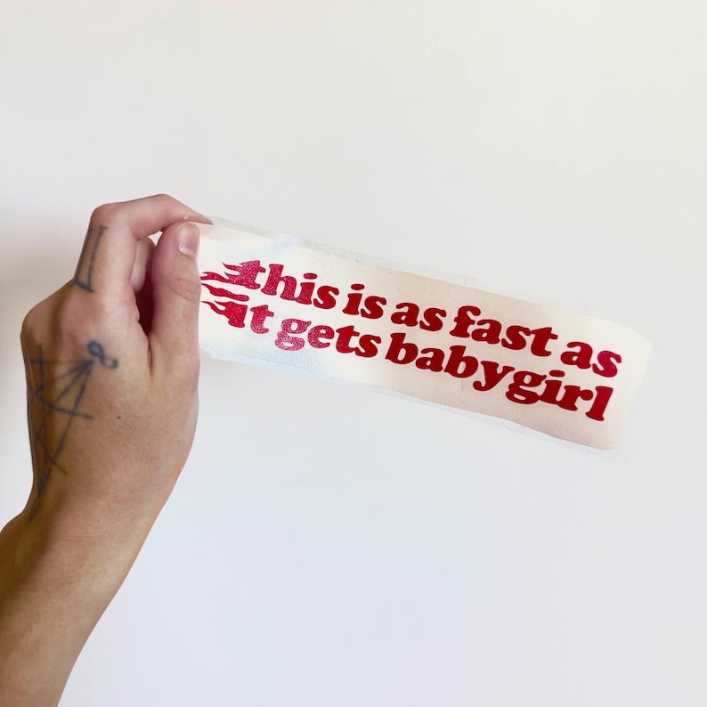 K&ouml;nnte beinhalten: Ein wei&szlig;er Aufkleber mit rotem Text, der "this is as fast as it gets babygirl" lautet. Der Text ist in einer fetten, serifenlosen Schriftart mit Flammengrafiken auf der linken Seite. Der Aufkleber wird vor einem wei&szlig;en Hintergrund gehalten.