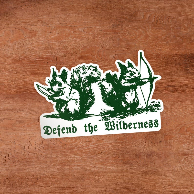 May include: A white sticker with a dark green illustration of two squirrels. One squirrel holds a knife, and the other holds a bow and arrow. Below the squirrels, the text reads "Defend the Wilderness" in a dark green, stylized gothic font.