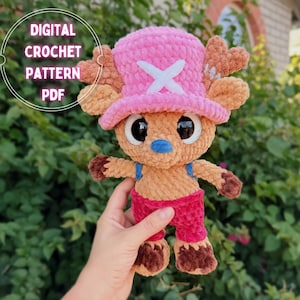 May include: A crochet plush toy featuring a tan creature with large black eyes, a blue nose, and brown hooves. It wears a bright pink hat with a white cross emblem and red pants. The text DIGITAL CROCHET PATTERN PDF is visible in the upper left corner.