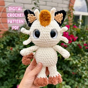 Op de afbeelding: Een crèmekleurige gehaakte knuffel met grote zwarte ogen, een goudbruine vlek op het voorhoofd, zwart-bruine oren en bruine voeten. De tekst "DIGITAL CROCHET PATTERN PDF" staat in het wit aan de linkerbovenkant van de afbeelding.