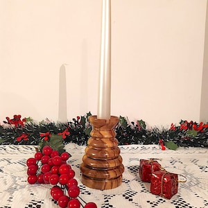 Può includere: Un portacandele in legno con una candela bianca, circondato da bacche rosse e una ghirlanda verde.