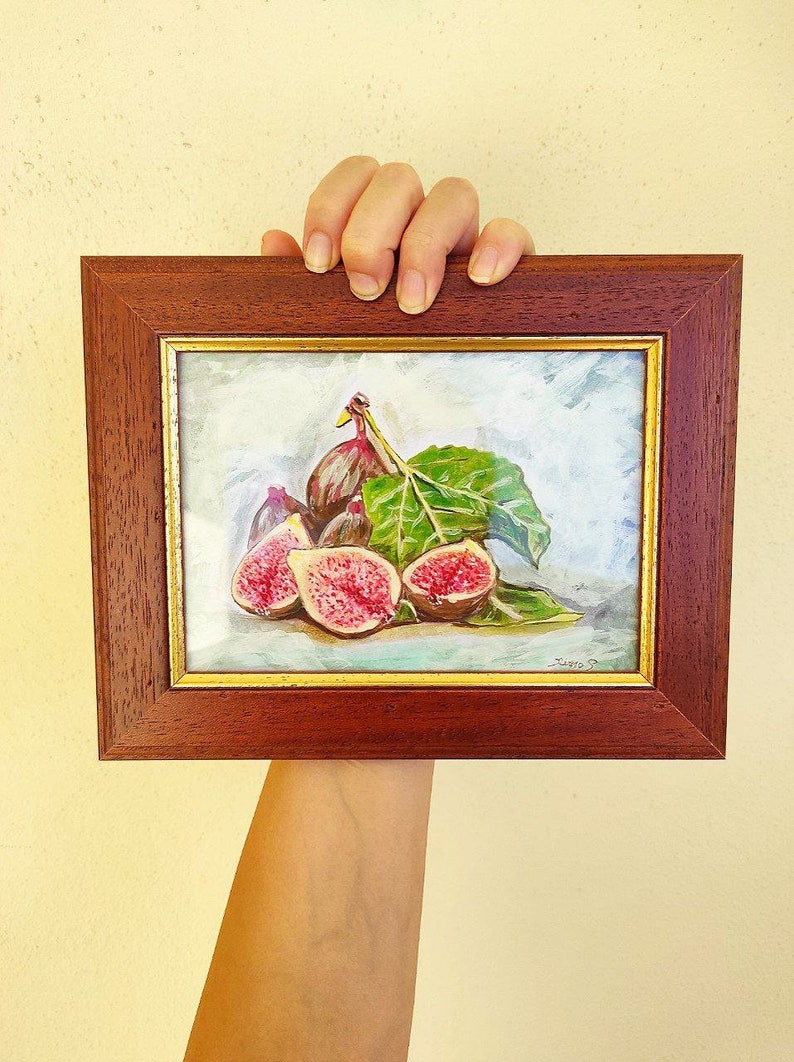 K&ouml;nnte beinhalten: Ein gerahmtes Gem&auml;lde eines Stilllebens mit einer Gruppe reifer Feigen und einem gr&uuml;nen Blatt. Die Feigen sind in Schattierungen von Lila, Rosa und Gr&uuml;n gemalt, und das Blatt ist ein leuchtendes Gr&uuml;n. Das Gem&auml;lde ist vor einem hellblauen Hintergrund platziert und in einem dunklen Holzrahmen gerahmt.