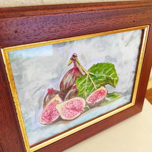 K&ouml;nnte beinhalten: Ein gerahmtes Aquarellbild eines Stilllebens mit Feigen. Das Bild zeigt eine Gruppe von Feigen, einige aufgeschnitten, mit einem einzelnen gr&uuml;nen Blatt. Die Feigen sind in Rosat&ouml;nen, Rot und Lila gemalt, mit einem realistischen Stil.