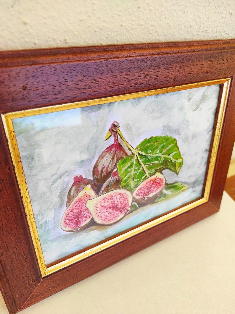 K&ouml;nnte beinhalten: Ein gerahmtes Aquarellbild eines Stilllebens mit Feigen. Das Bild zeigt eine Gruppe von Feigen, einige aufgeschnitten, mit einem einzelnen gr&uuml;nen Blatt. Die Feigen sind in Rosat&ouml;nen, Rot und Lila gemalt, mit einem realistischen Stil.