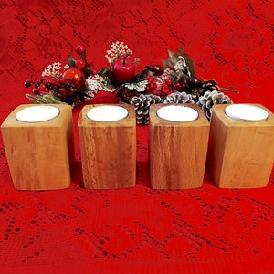 Può includere: Quattro portacandele in legno con finitura in legno naturale. Ogni portacandele contiene una piccola candela rotonda bianca. I portacandele sono disposti in fila su una tovaglia rossa di pizzo.