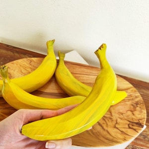 Könnte beinhalten: Vier gelbe Holzbananen in einer Holzschale. Die Bananen sind mit einem gelben und weißen Marmormuster bemalt.