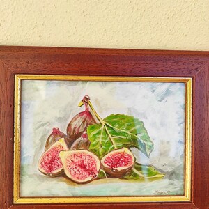 K&ouml;nnte beinhalten: Ein gerahmtes Aquarellbild eines Stilllebens mit Feigen. Das Bild zeigt eine Gruppe von Feigen, einige ganz und einige aufgeschnitten, mit einem gr&uuml;nen Blatt. Der Hintergrund ist hellblau mit einer wei&szlig;en W&auml;sche. Das Bild ist unten rechts mit "Zino" signiert.