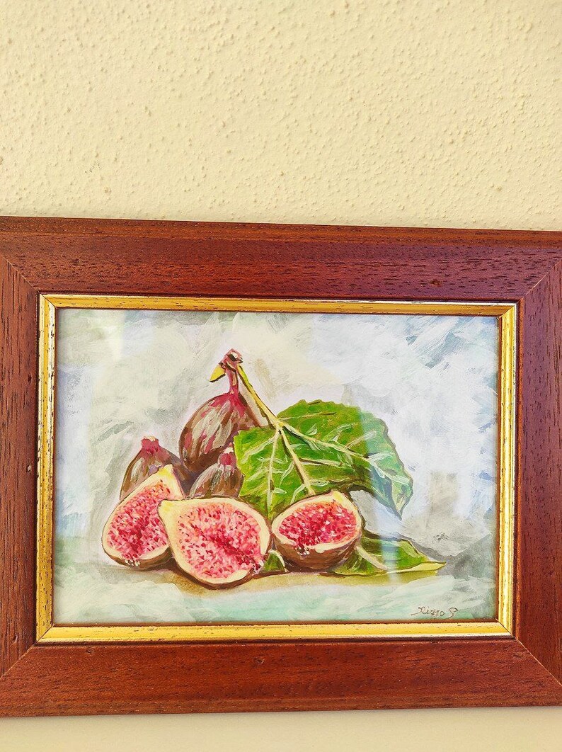 K&ouml;nnte beinhalten: Ein gerahmtes Aquarellbild eines Stilllebens mit Feigen. Das Bild zeigt eine Gruppe von Feigen, einige ganz und einige aufgeschnitten, mit einem gr&uuml;nen Blatt. Der Hintergrund ist hellblau mit einer wei&szlig;en W&auml;sche. Das Bild ist unten rechts mit "Zino" signiert.