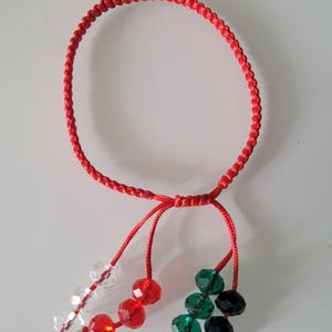 Könnte beinhalten: Rotes geflochtenes Armband mit hängenden facettierten Perlen in Klar, Rot, Grün und Schwarz. Das Armband besteht aus roter Kordel und verfügt über einen Schiebeknotenverschluss. Ein einfaches, farbenfrohes Accessoire.