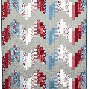 May include: A patchwork quilt with a grey background and a repeating pattern of red, white, and blue rectangular blocks. The blocks feature floral, polka dot, and striped patterns. The quilt is edged with a dark blue binding.