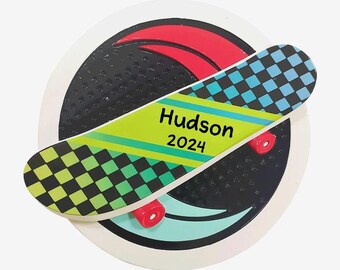 May include: A white and black skateboard ornament with a green and blue checkered design. The skateboard has the name "Hudson" and the year "2024" written on it.