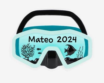 Op de afbeelding: Een blauwe en witte duikbril kerstversiering met de tekst "Mateo 2024" aan de voorkant. De bril heeft een zwarte neusbrug en een zwarte band.