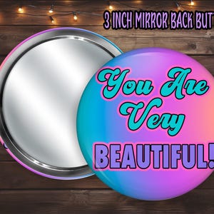 May include: A 3 inch mirror back button with a gradient background of pink, blue, and purple. The text "You Are Very Beautiful!" is written in a stylised font with turquoise and pink outlines.