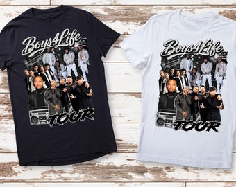 May include: Two t-shirts, one black and one white, featuring a graphic design. The design includes the text "Boys4Life" above a group of people and the word "TOUR" below. The shirts are displayed on a light brown wooden surface.