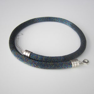 Op de afbeelding: Een zwarte kralenketting met iriserende kralen en zilveren magneetsluitingen.